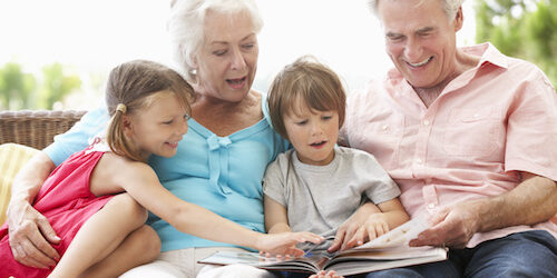 Grandparents And Grandchildren Reading Book On Garden Seat